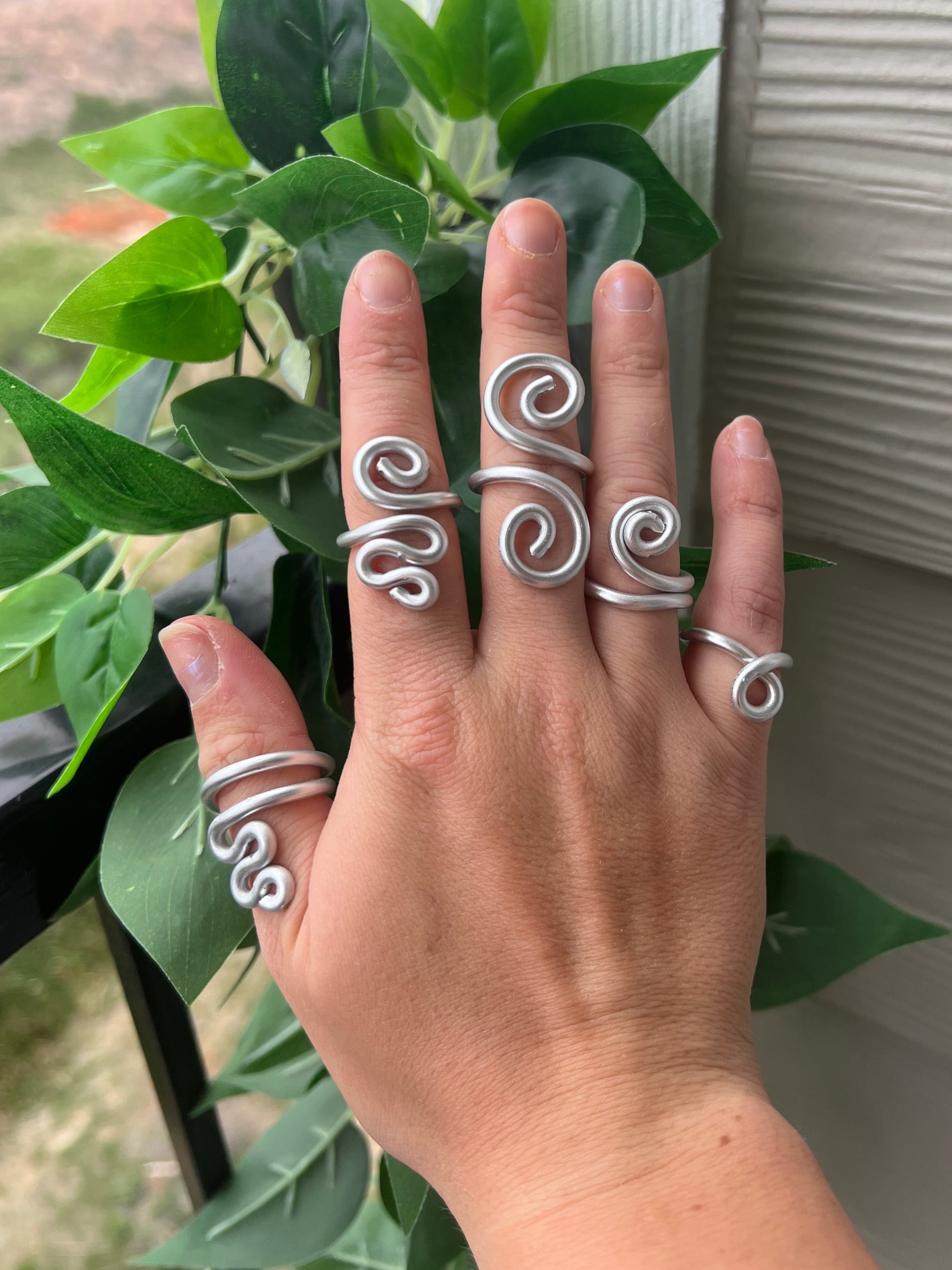 Hand wearing multiple silver rings with a plant in the background