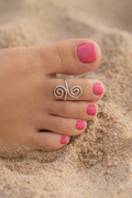 Close-up of a foot with pink nail polish wearing a silver toe ring on a sandy background