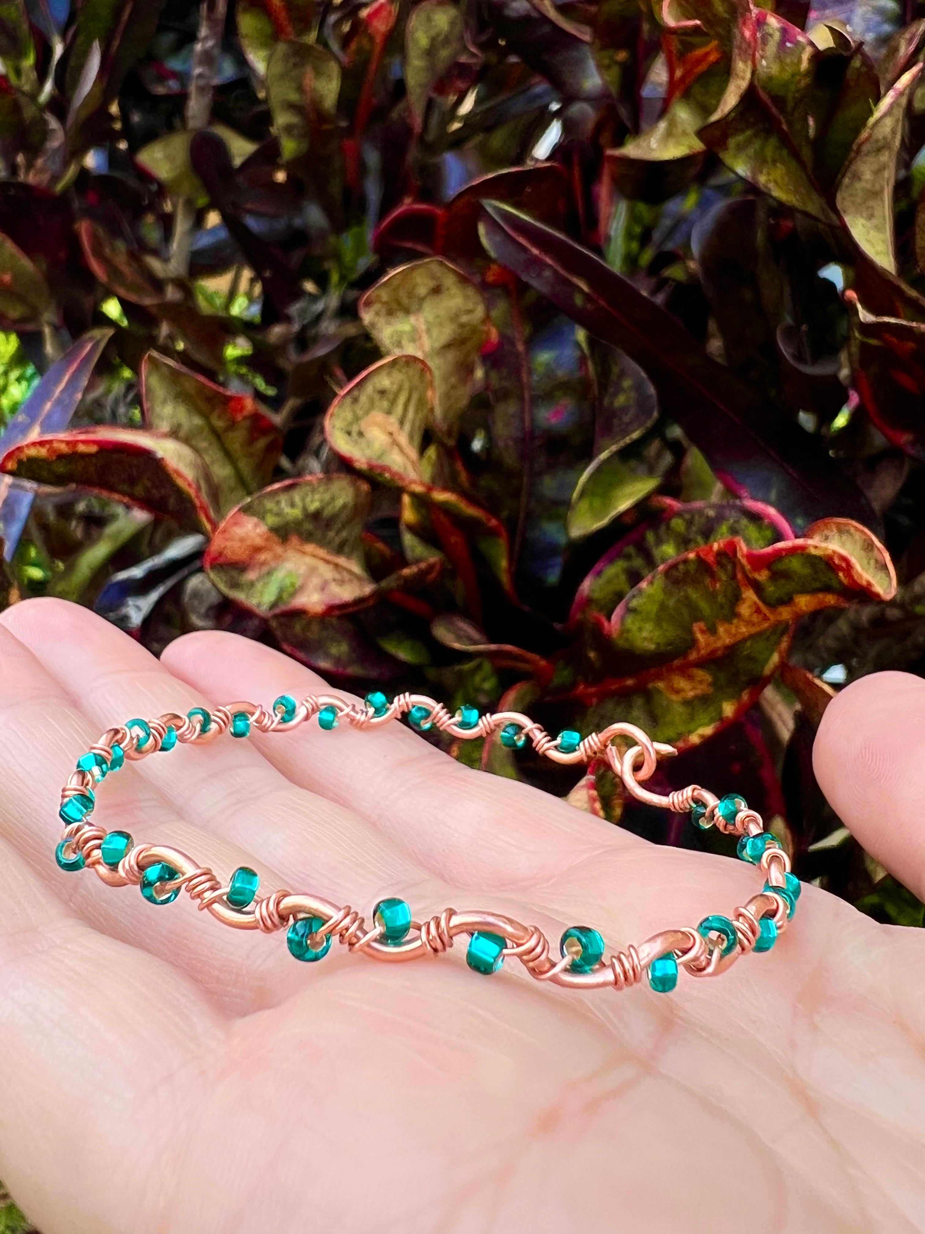 Copper bracelet with turquoise beads on a hand against a leafy background