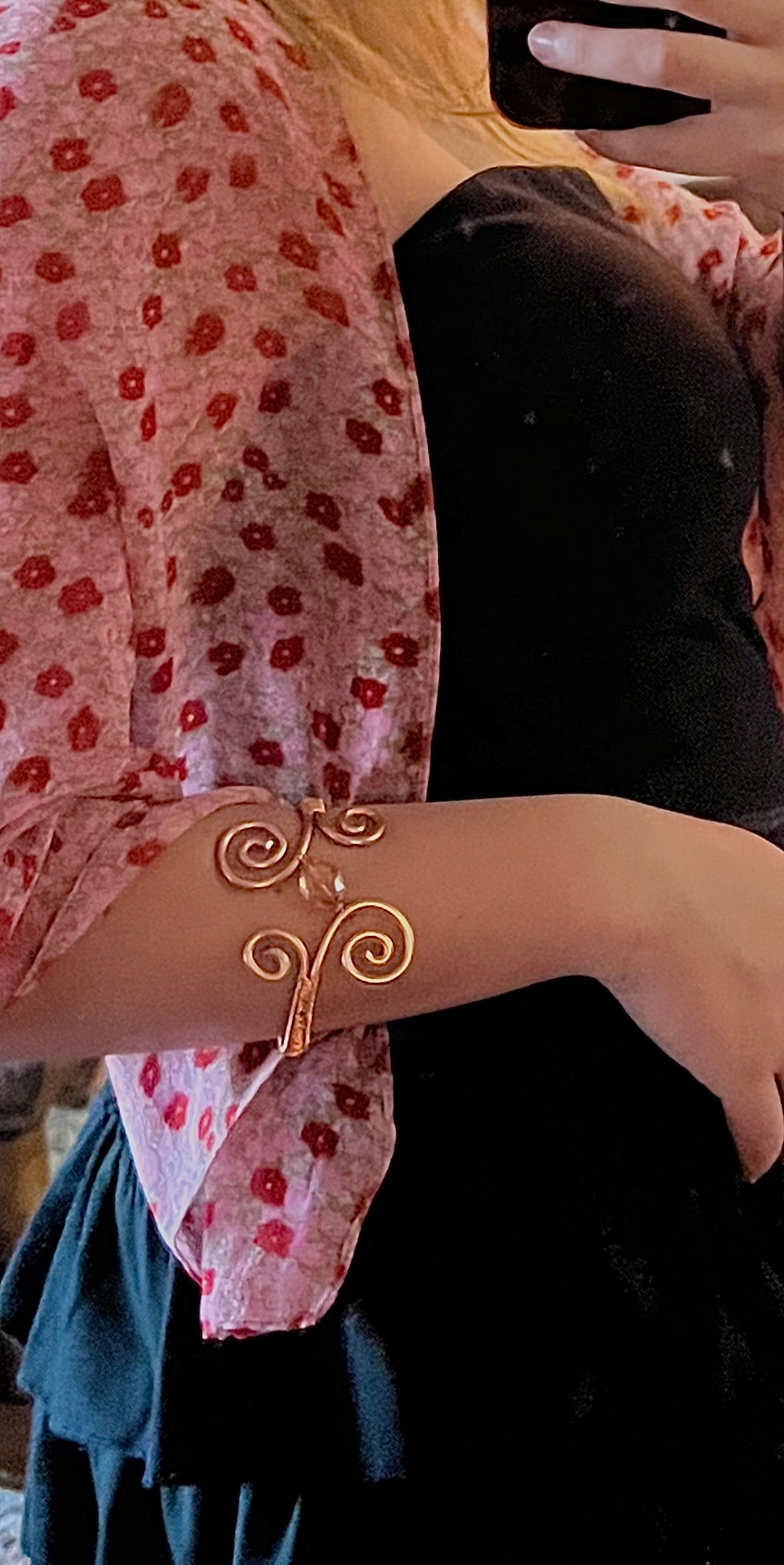 Close-up of a person wearing a gold bracelet with a floral-patterned garment.