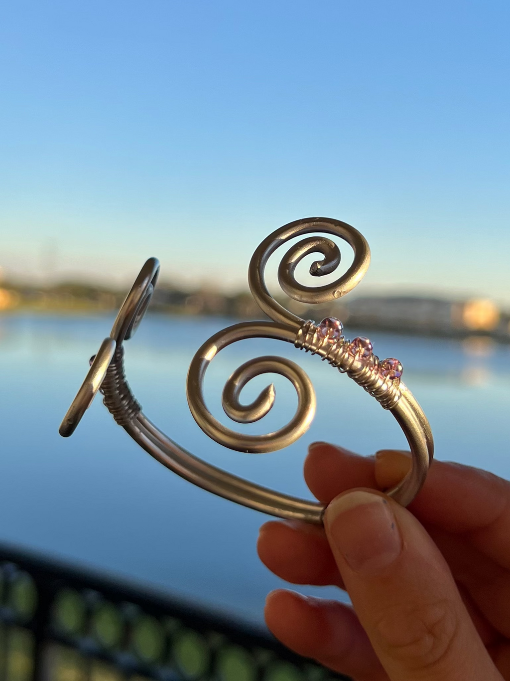 Hand holding a decorative metal object with a spiral design against a scenic background of water and sky.