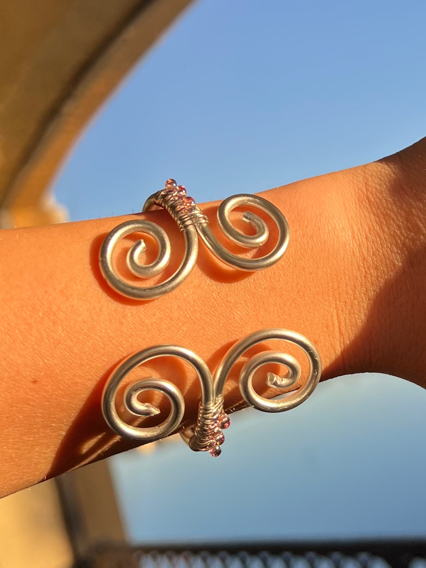 Close-up of a wrist wearing a silver spiral bracelet with a blurred outdoor background
