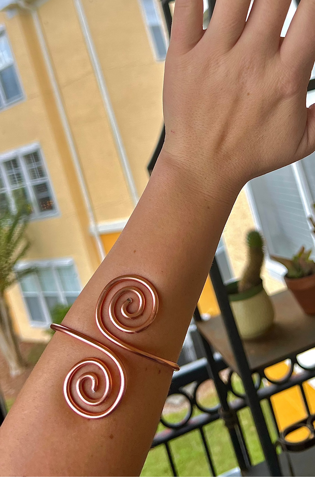 Hand wearing a copper spiral bracelet with a blurred outdoor background