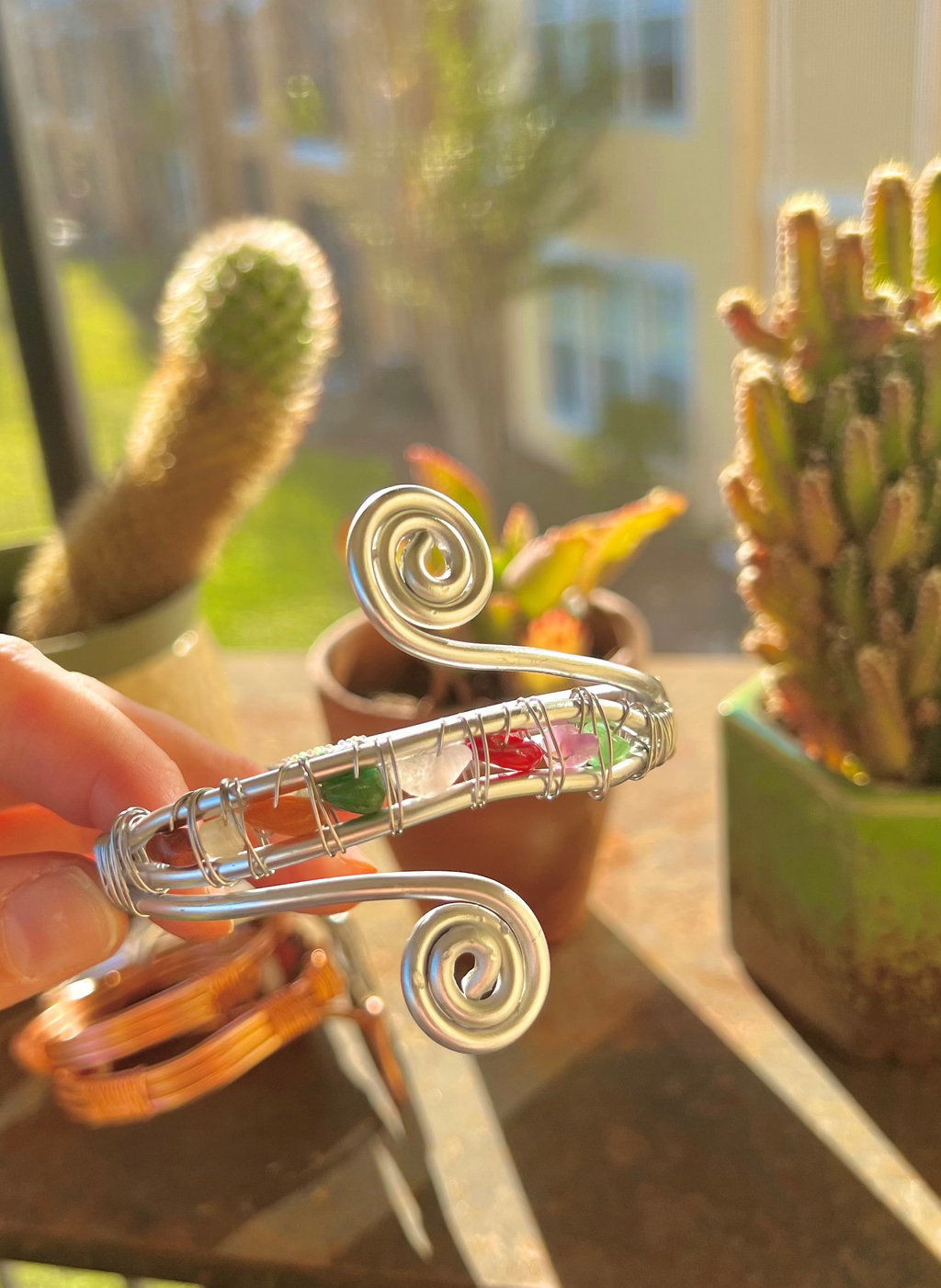Silver bracelet with colorful stones held in front of potted cacti