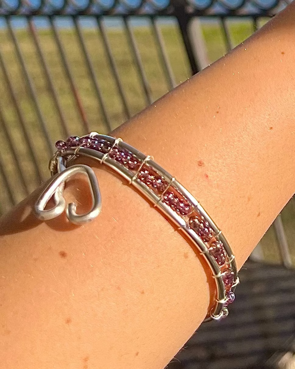 Silver bracelet with pink stones on a person's wrist against a blurred outdoor background