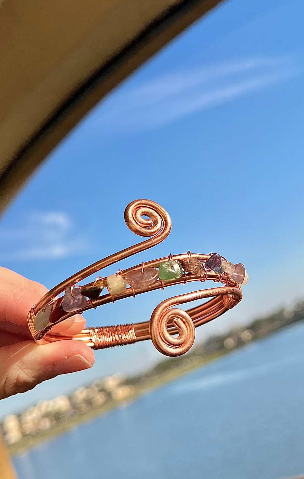 Copper bracelet with embedded stones held by a hand against a blurred outdoor background