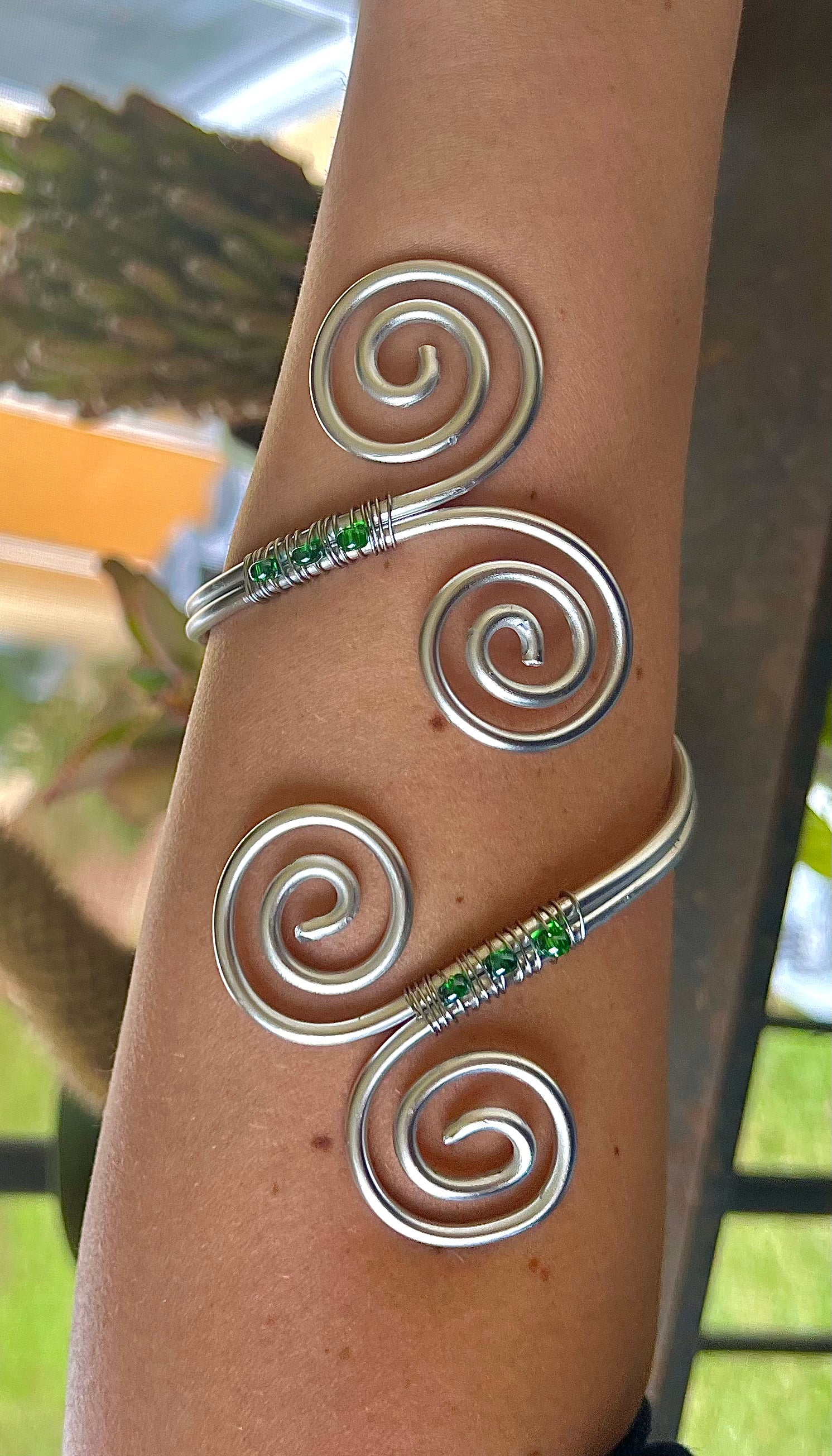 Silver spiral arm band with green stones on a person's arm against a blurred outdoor background