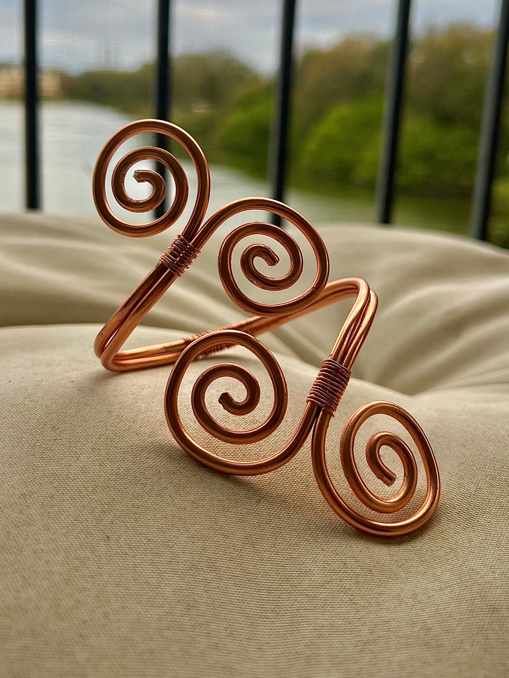 Copper spiral bracelet on a beige surface with a blurred outdoor background