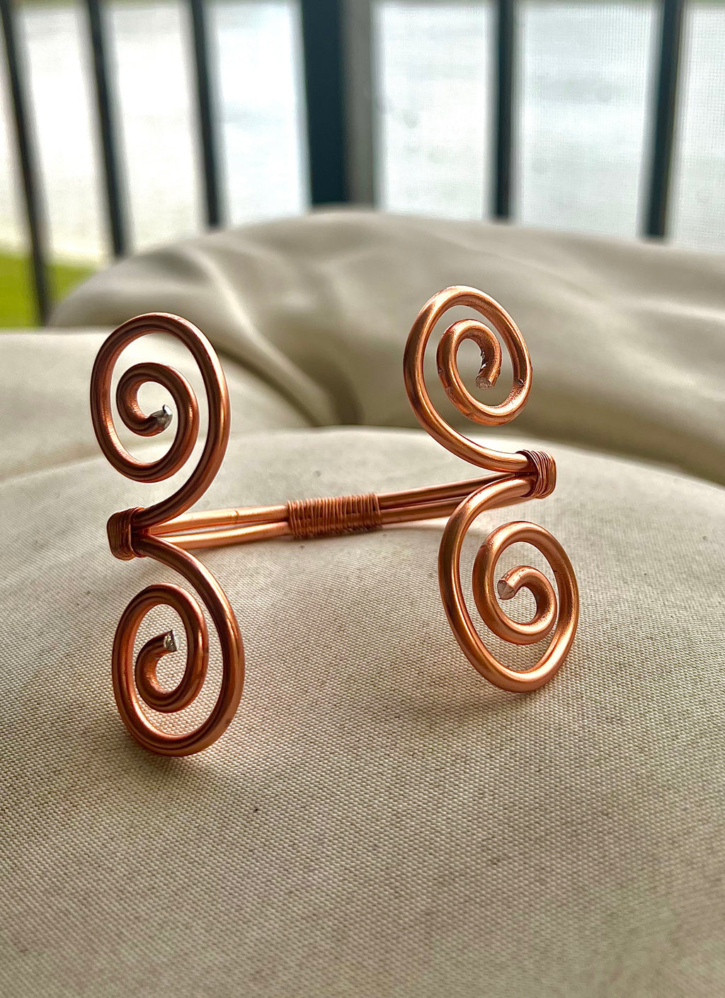 Decorative copper harm cuff on a textured surface with blurred background