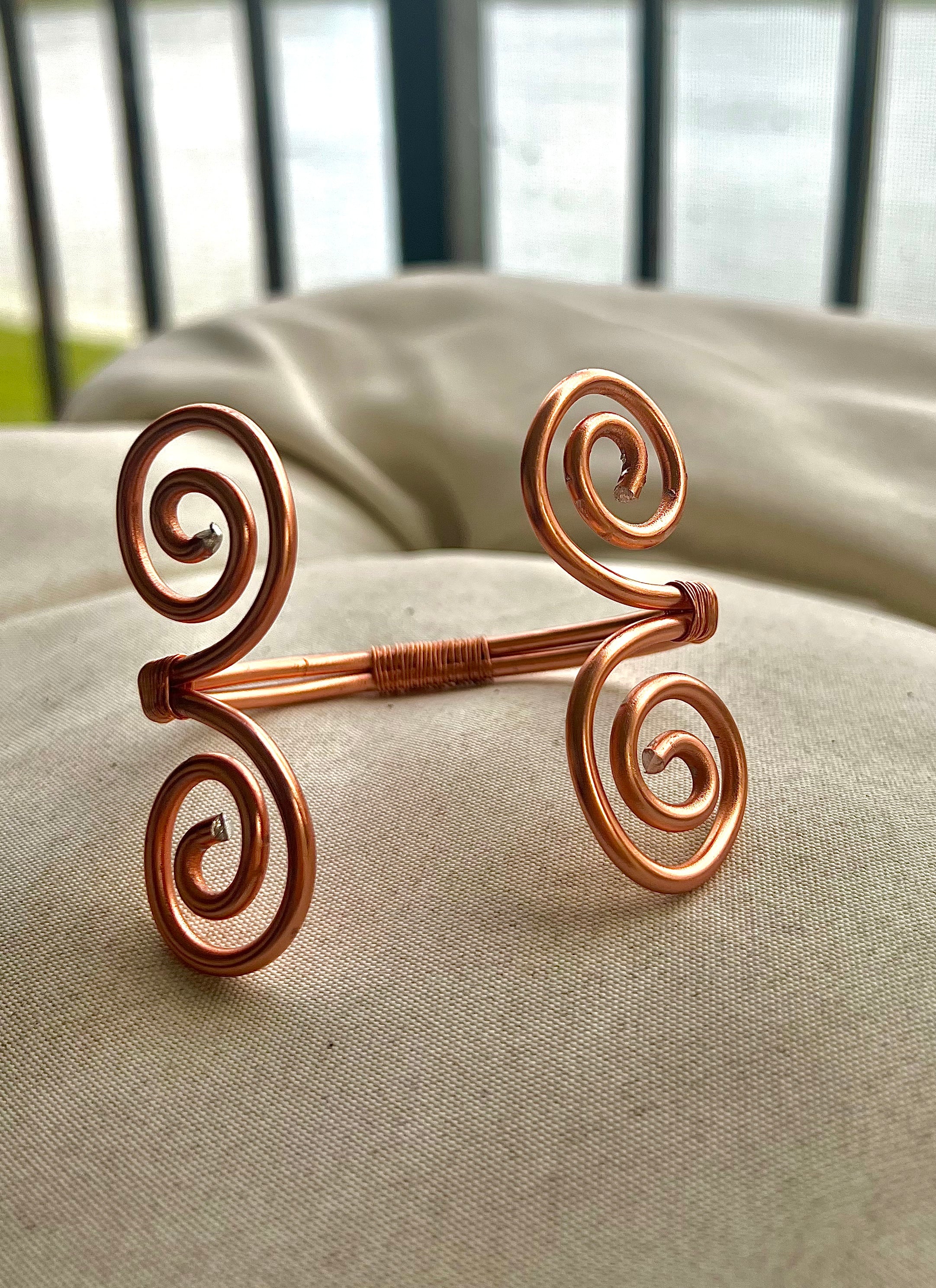 Decorative copper harm cuff on a textured surface with blurred background