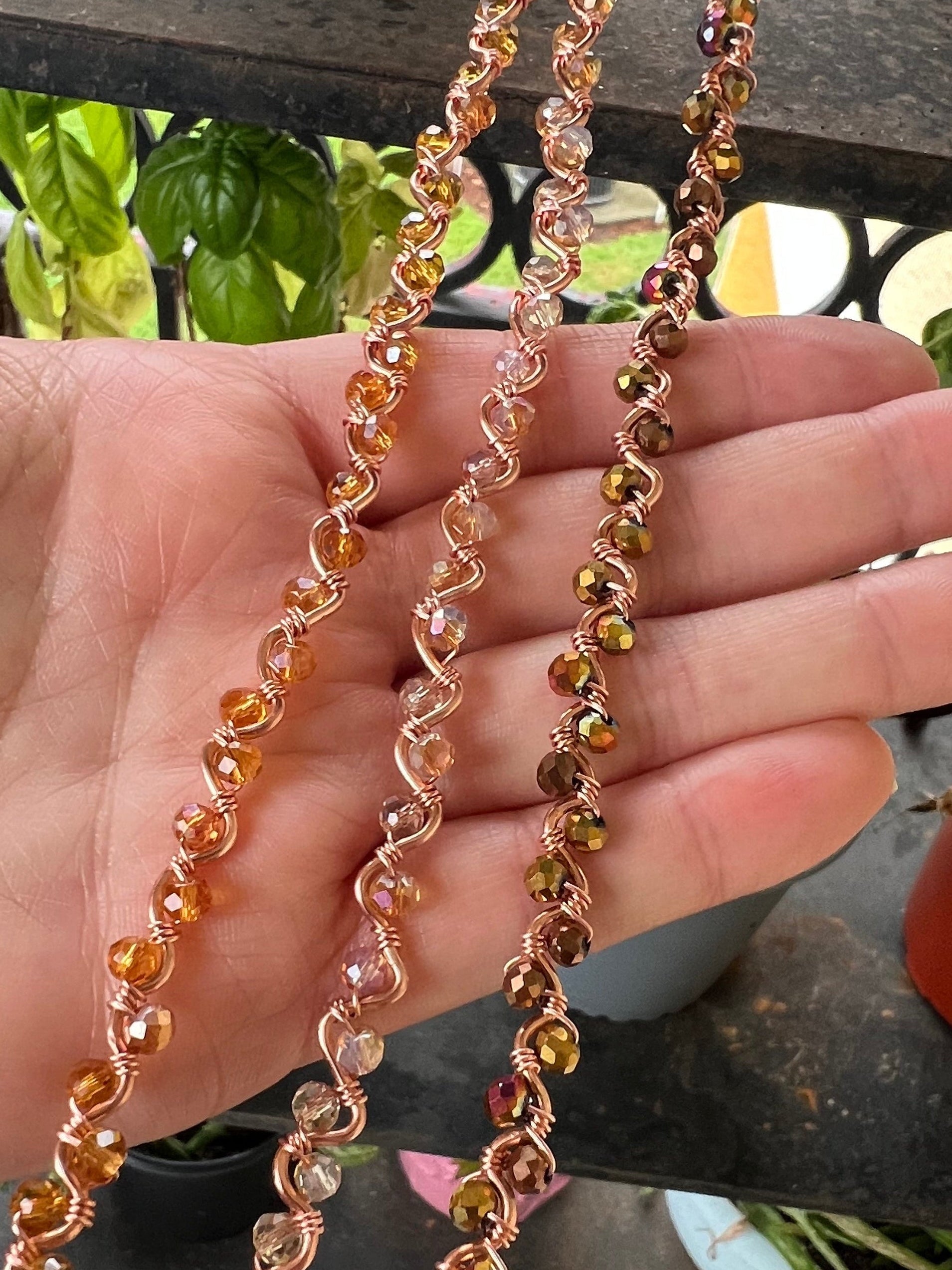 Hand holding a beaded chain with a garden background