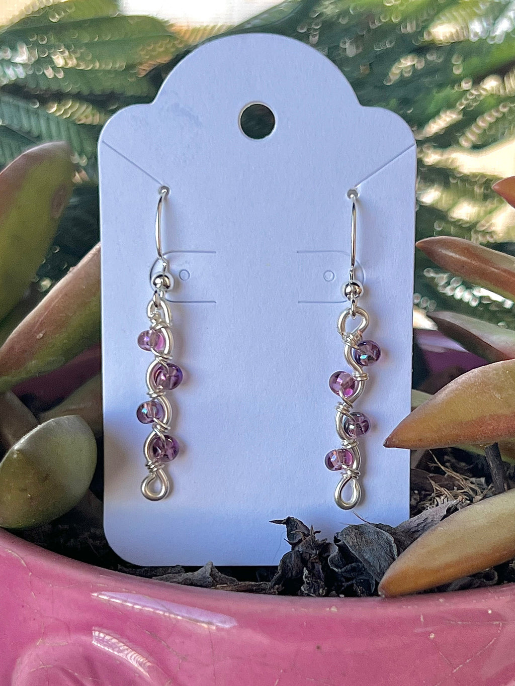 Pair of pink beaded earrings on a white card with a plant in the background