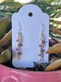 Pair of pink beaded earrings on a white card with a plant in the background