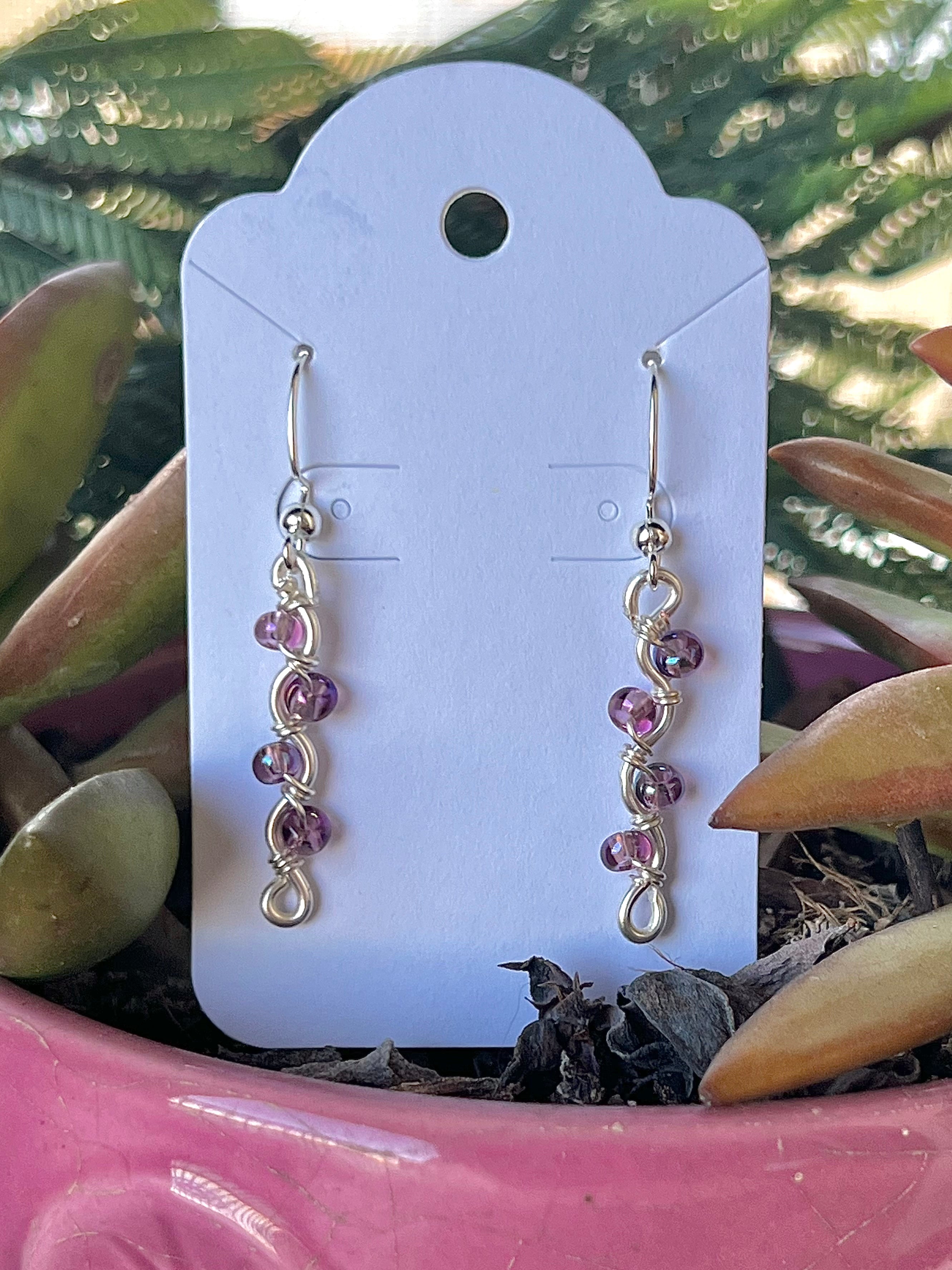 Pair of pink beaded earrings on a white card with a plant in the background