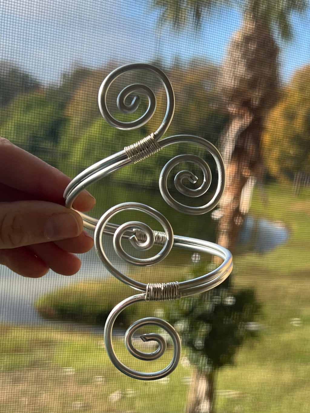 Hand holding a decorative metal object with spiral designs against a reflective glass surface.