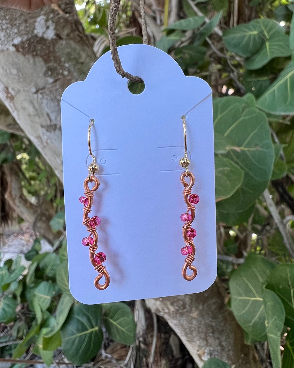 Pair of gold and pink beaded earrings on a purple card with a natural background
