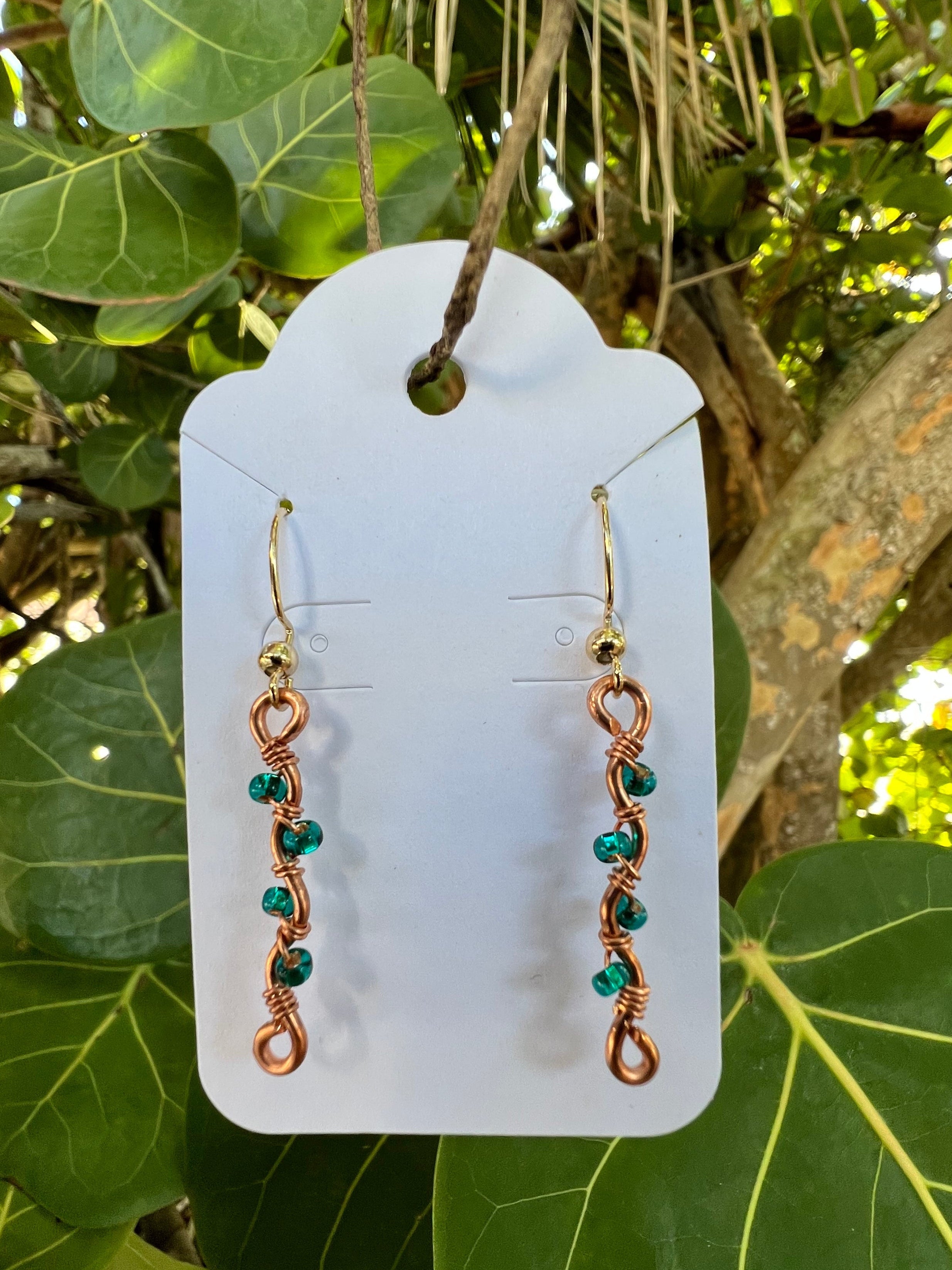 Pair of copper and green bead earrings on a white card with a natural background