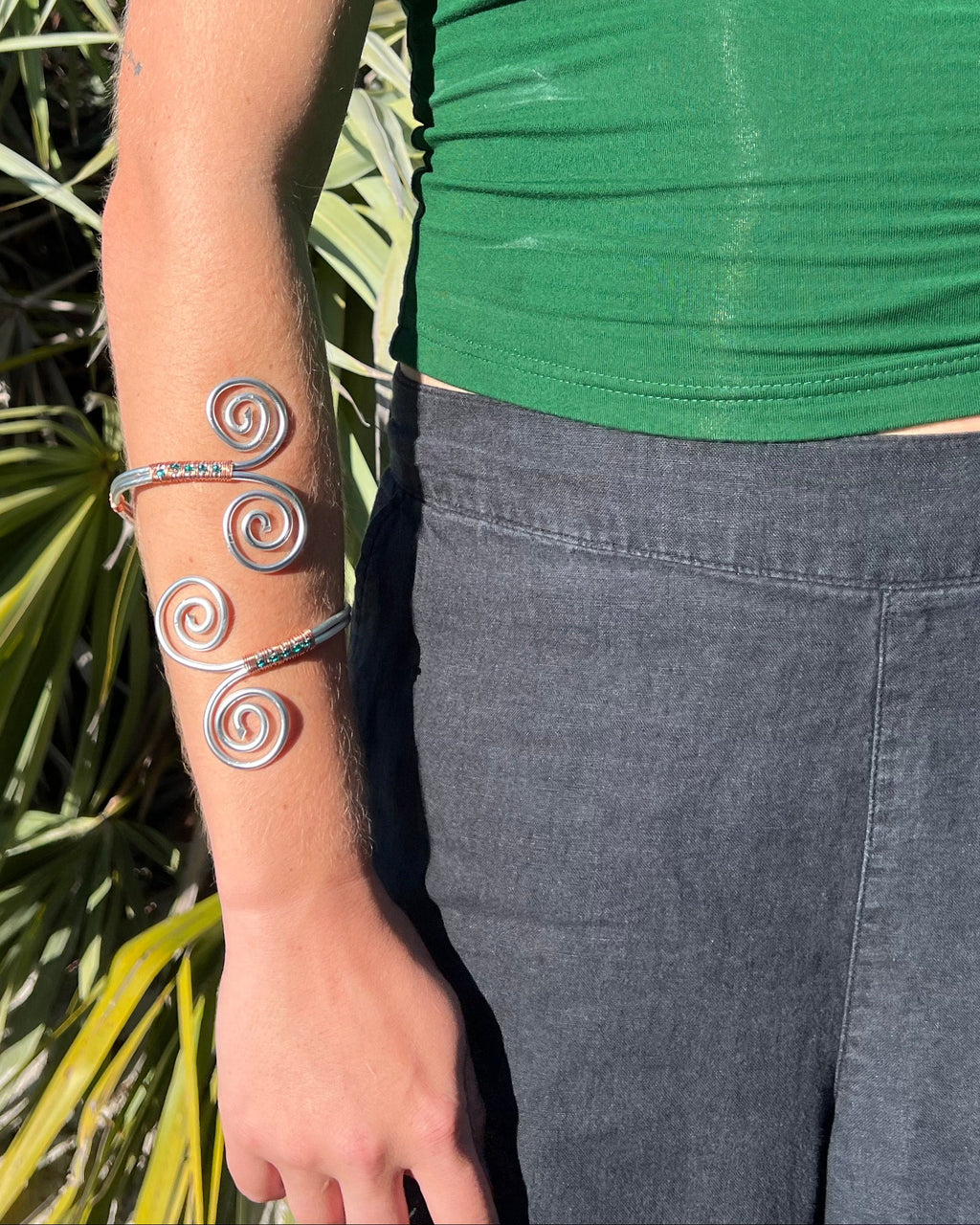 Person wearing a green top and dark pants with a bracelet on a natural background