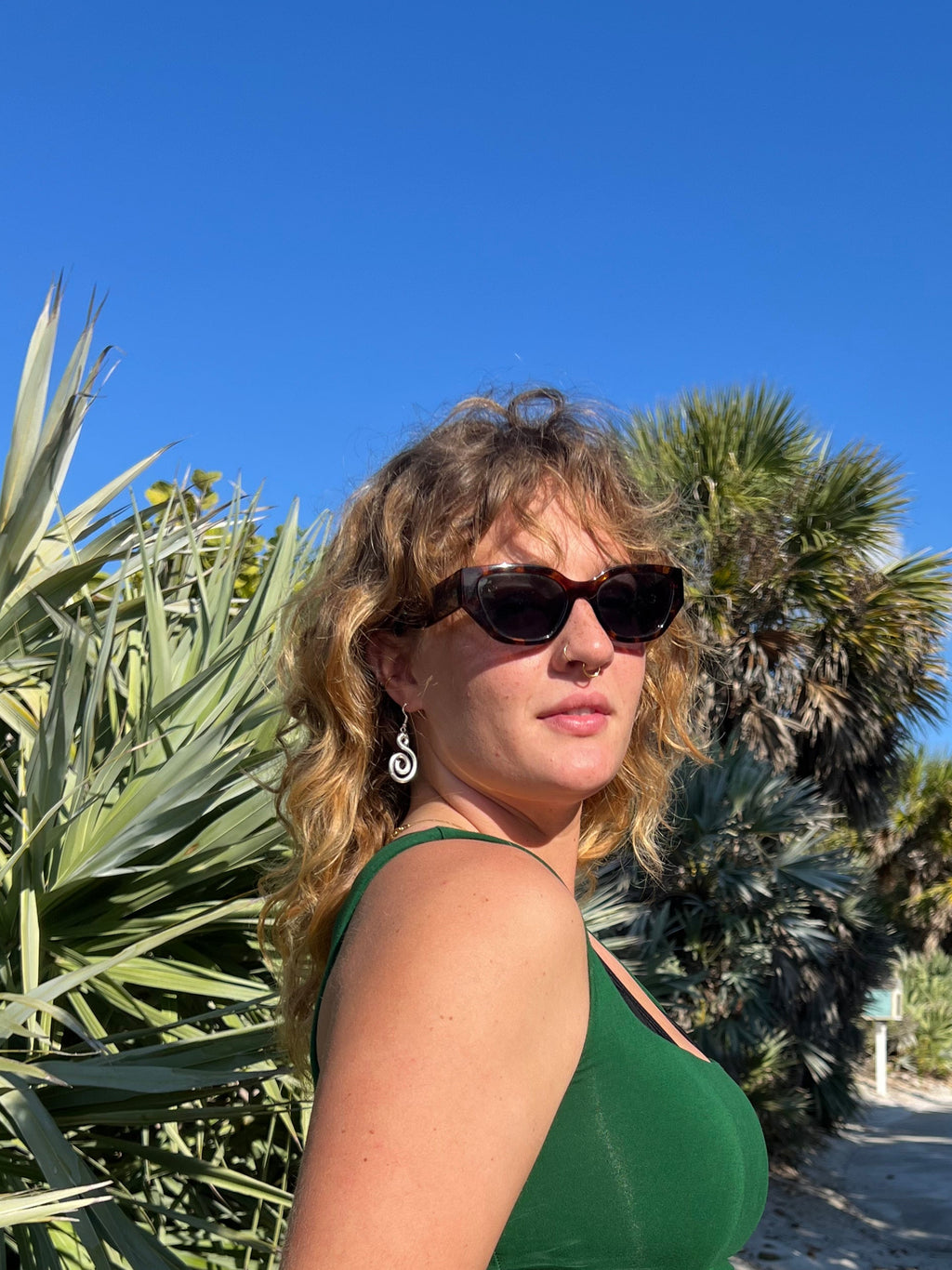 Person standing outdoors with palm trees and clear blue sky wearing spiral earrings