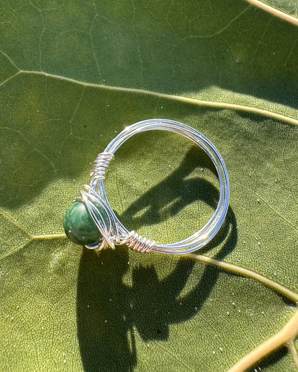 Silver ring with a green stone on a green leaf