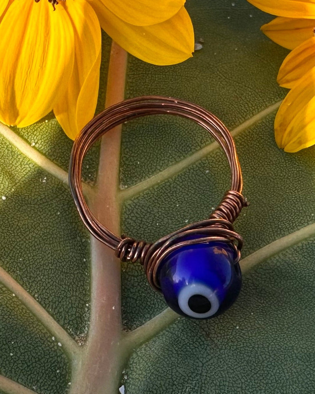 Two yellow flowers on a large green leaf with a copper ring featuring a blue stone.