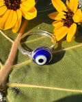Silver ring with a blue evil eye charm on a green leaf with yellow flowers.