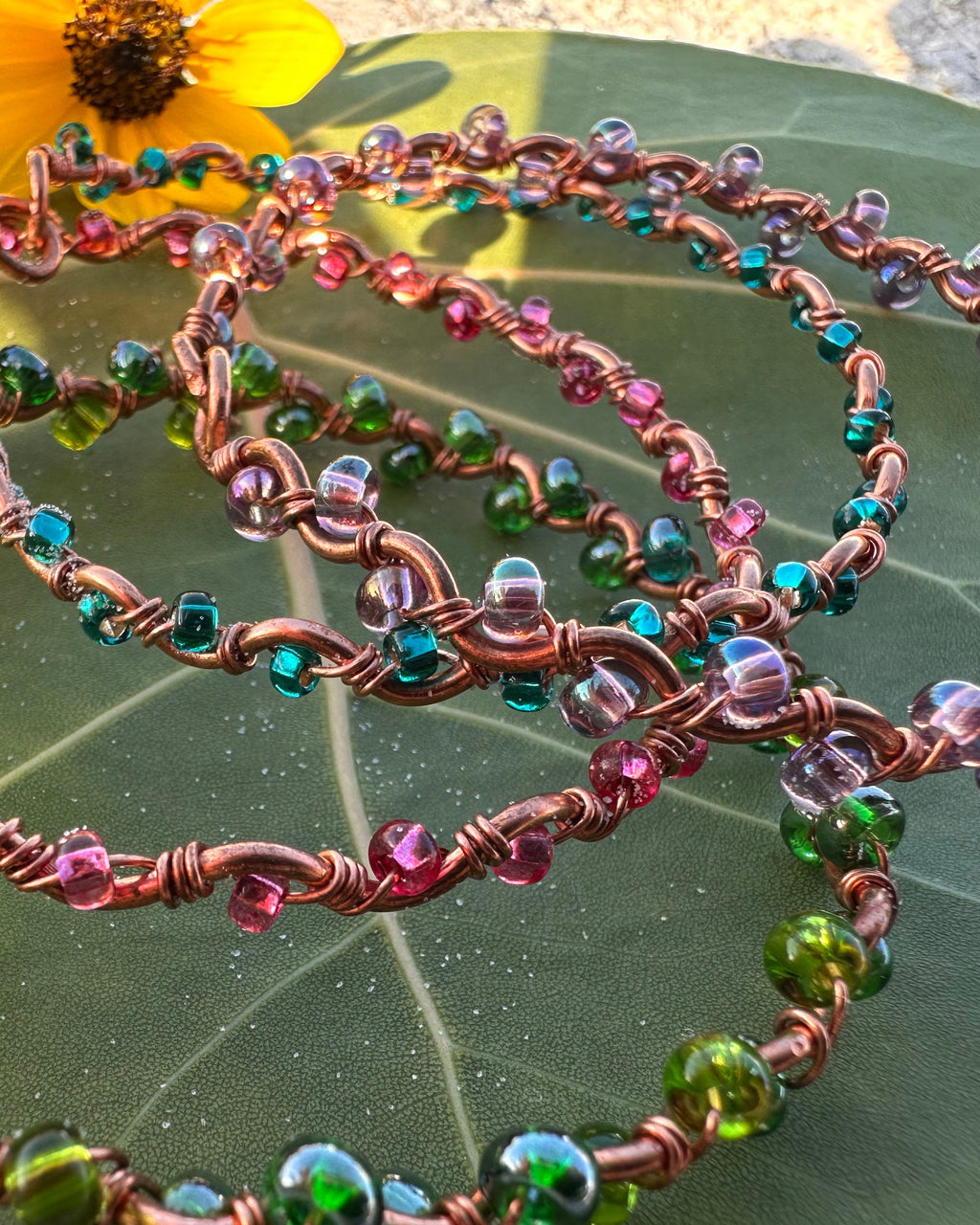 Colorful beaded necklace on a green leaf with yellow flowers in the background
