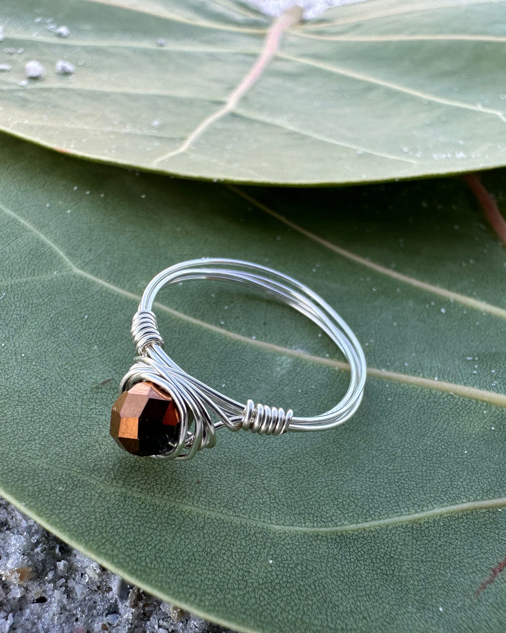 Silver wire-wrapped ring with a brown gemstone on a green leaf