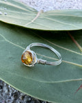 Silver ring with a yellow gemstone on a green leaf