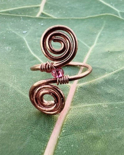Copper spiral ring with a pink gemstone on a green leaf background