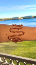 Person wearing a copper bracelet with a scenic background of water and greenery