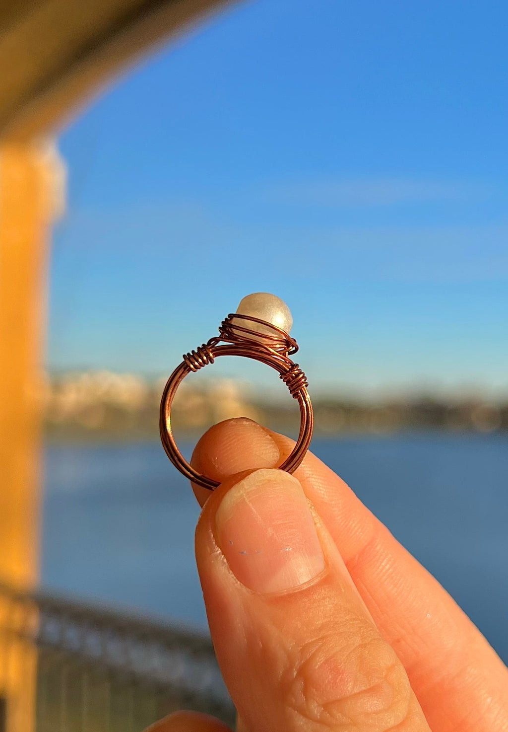Hand holding a ring with a pearl against a blurred outdoor background